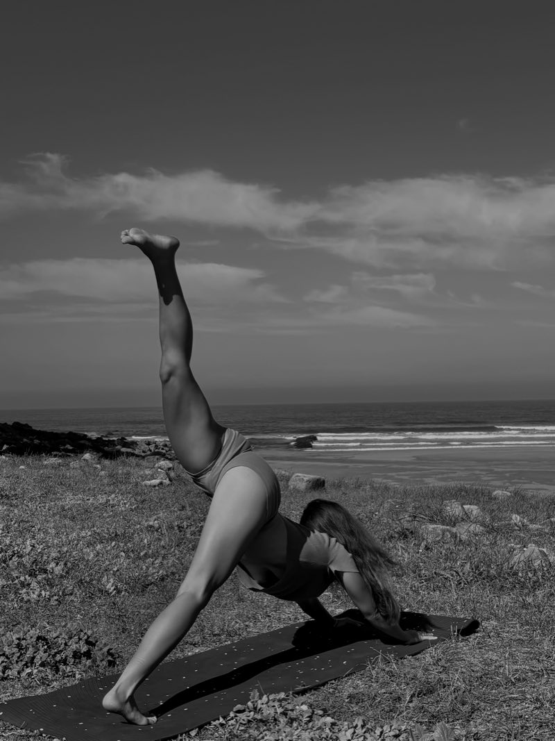 Paula in a yoga pose by the sea, one leg raised high, wearing the cotton shorts