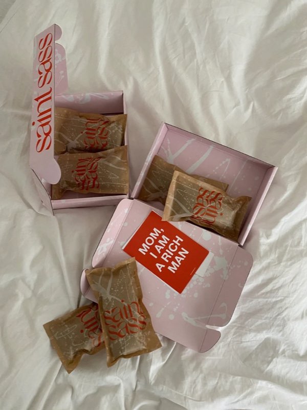 Saint Sass packaging: pink boxes, kraft-paper parcels and a red card reading Mom, I am a rich man